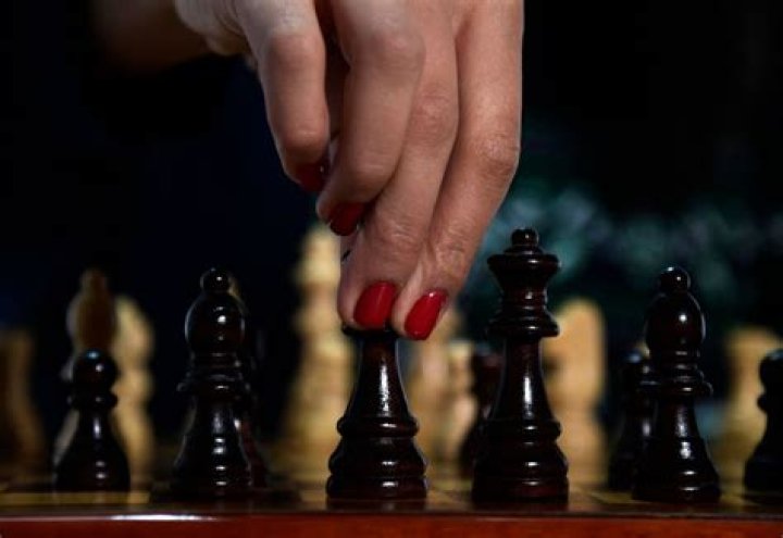 Fingers touching a chess piece. The nails are painted red.